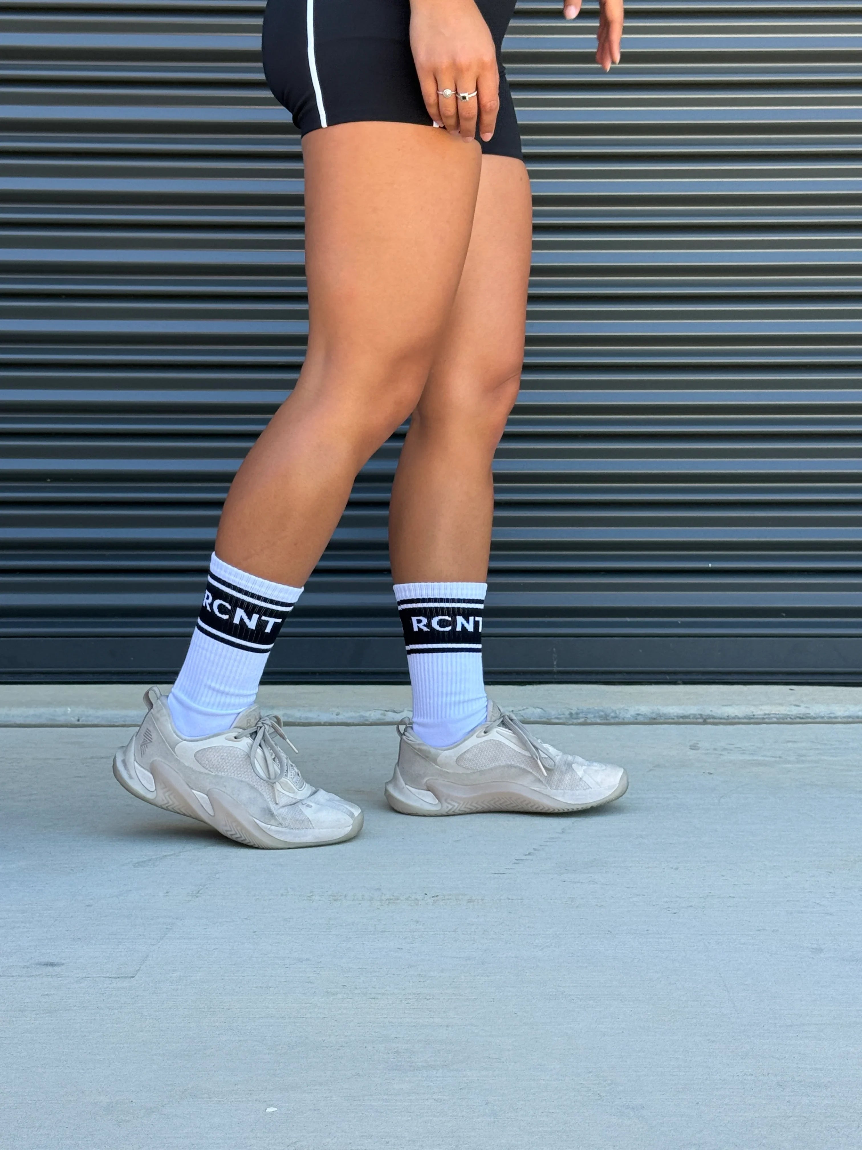 Person wearing white RCNT branded athletic socks and white sneakers standing on concrete