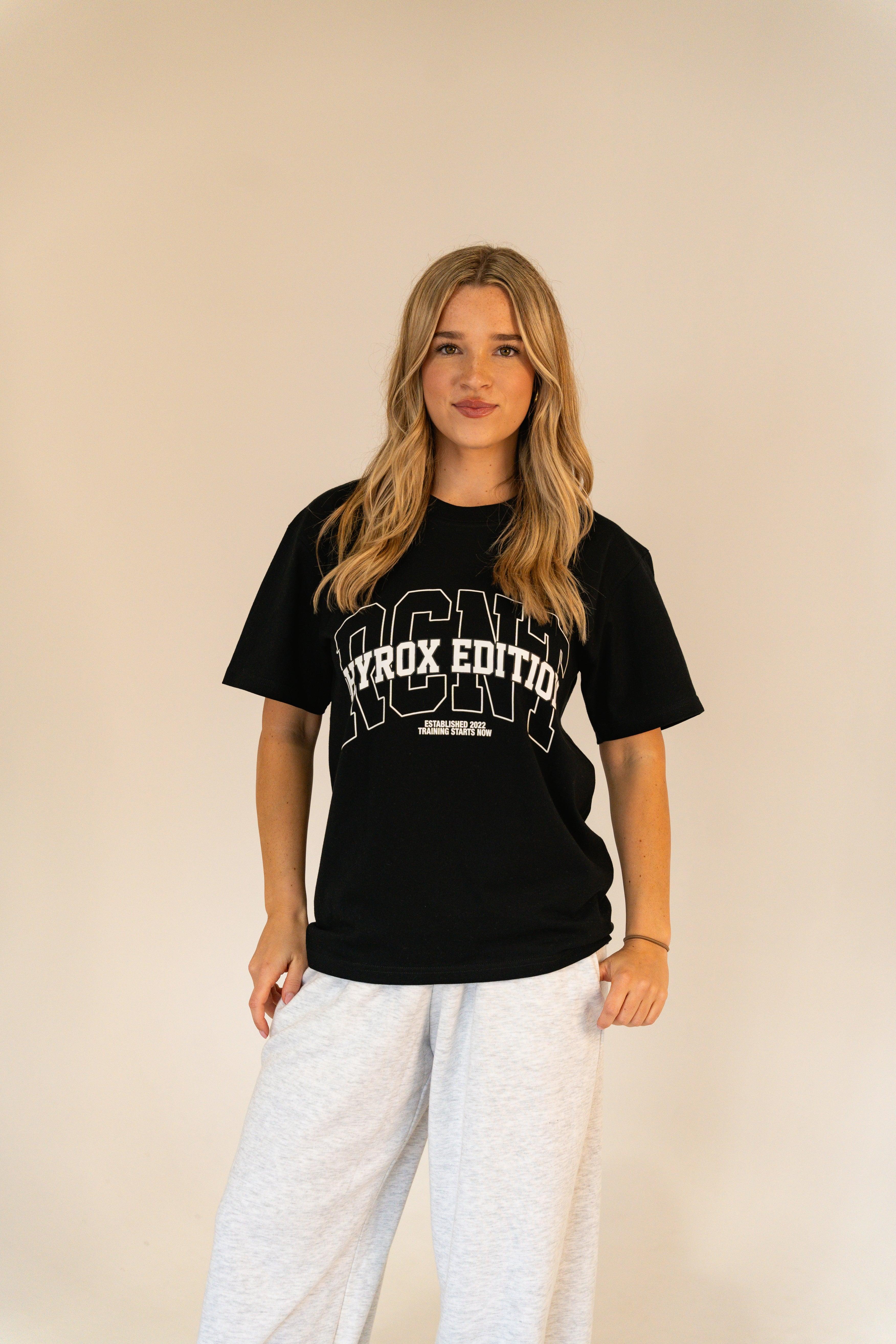 Woman wearing black ICON Hyrox Edition T-shirt and light gray sweatpants against beige background