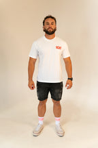 Man wearing white RCNT logo t-shirt, black distressed shorts, white RCNT socks, and white sneakers on plain background
